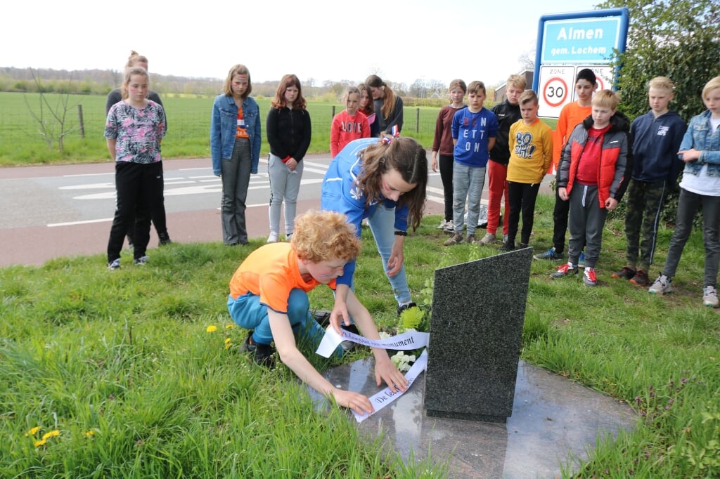 Teun Rouwenhorst, links, legt met Rosalie Crum (r) het boeket bij het monument terwijl de klas toekijkt. Foto: Arjen Dieperink