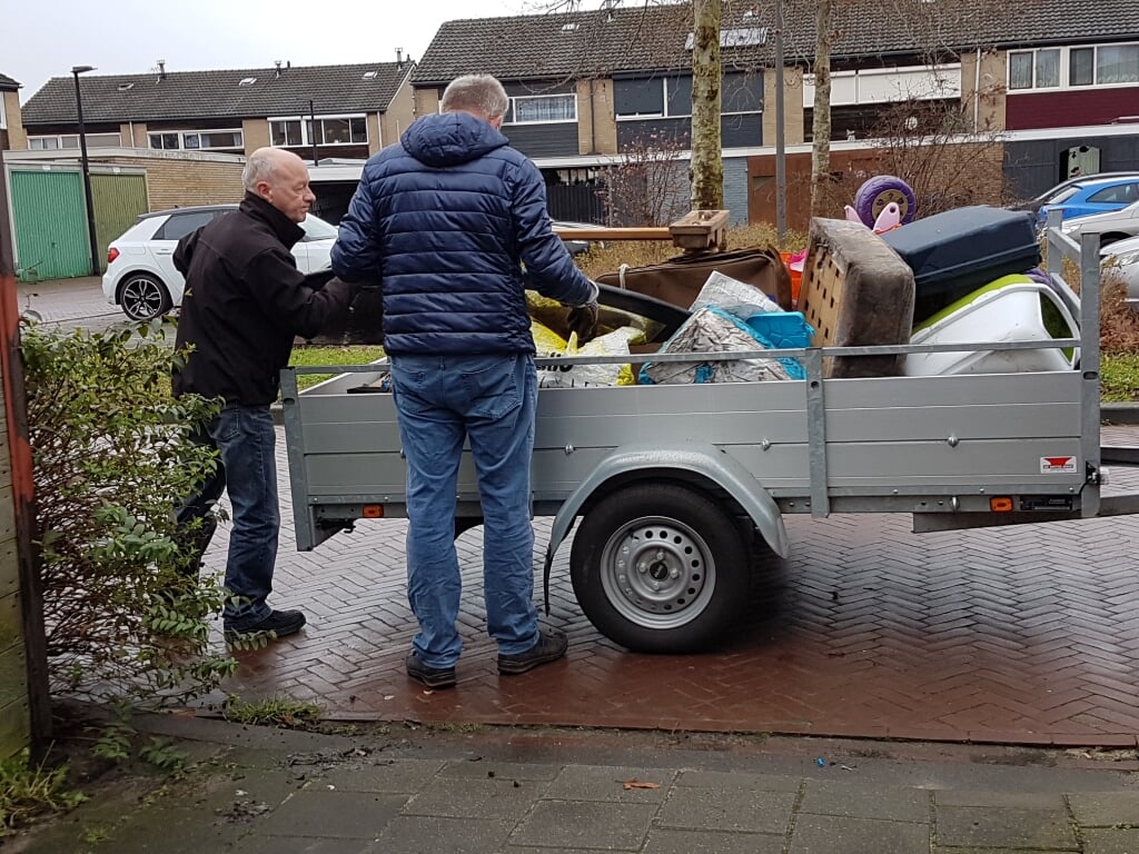 Twee vrijwilligers laden een aanhangwagen vol tijdens een opruimklus. Foto: Present Winterswijk