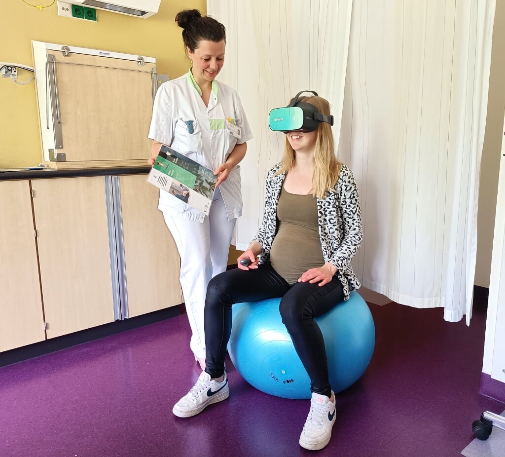 Obstetrieverpleegkundige Lotte Kroeze-Roolvink helpt een zwangere patiënt bij het gebruik van de VR-bril. Foto: PR SKB