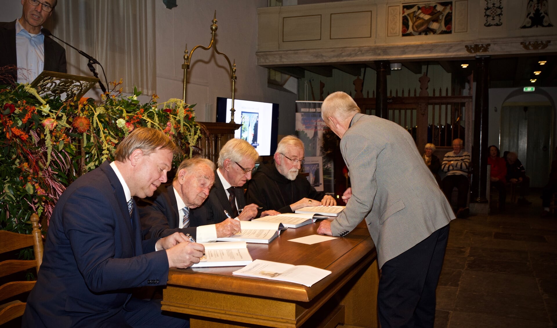 Een uniek plaatje! Vlnr. wethouder Rob Opdam, ds Ph. Ouwendijk pastoor H. Helsloot, abt G. Mathijsen krijgen van Jaap de Graaf de boeken ter ondertekening aangereikt.