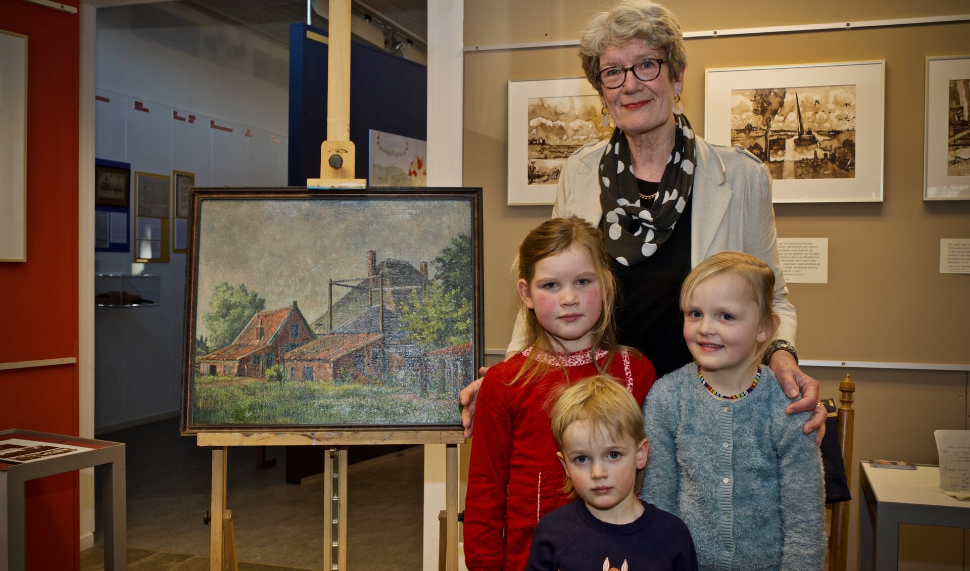 Jannie Baltus-Dekker met het gerestaureerde schilderij van haar vader. Voor Jannie Baltus-Dekker drie van haar vier kleinkinderen, Saar Ruigewaard, Poppy Baltus en Midas Baltus. Robin Langedijk was helaas verhinderd.