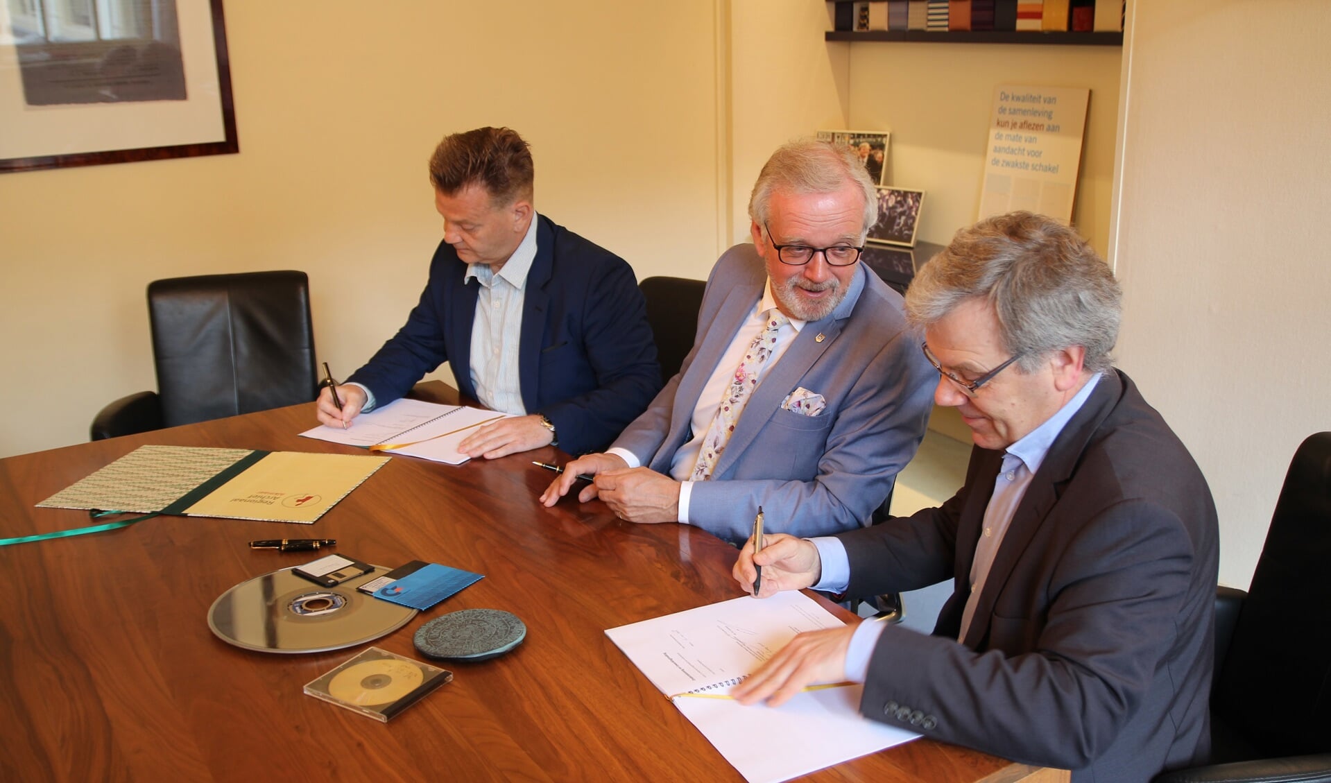Mark Lindeman (Picturae), Alkmaarse burgemeester Bruinooge (Alkmaar) en Paul Post (Regionaal Archief) ondertekenden de overeenkomst met softwareaanbieder Picturae. Op tafel verschillende informatiedragers. Foto Regionaal Archief Alkmaar. 
