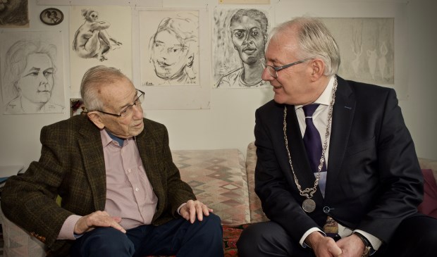 De jarige heer Naessens in gesprek met burgemeester Hans Romeyn. Op de achtergrond enkele tekeningen getekend door de heer Naessens.