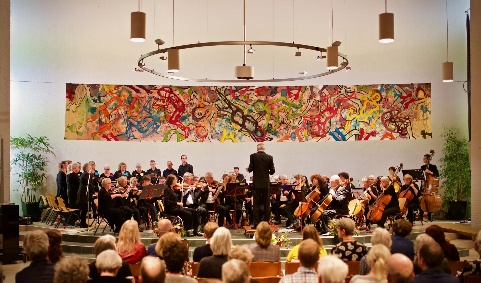 Het Arnhems Symfonie Orkest NOVA en het Peace Opus koor onder het kunstwerk van Annemarie Kuster.