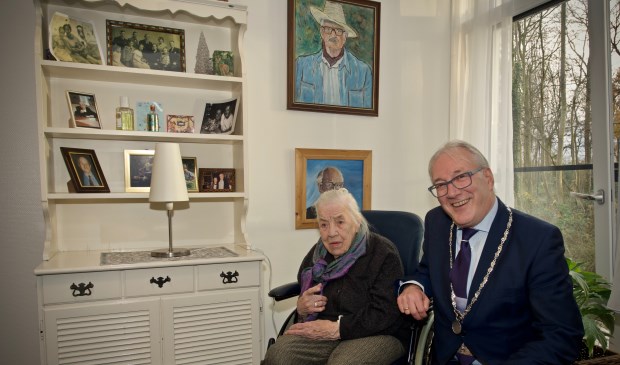 Mevrouw Hulsman samen met burgemeester Hans Romeyn bij een kast met de vele foto's en schilderijen geschilderd door meneer Hulsman.