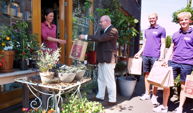 Wethouder Fred Dellemijn overhandigt het ‘We zijn er voor elkaar’ promotiepakket aan eigenaresse Kim van Bloemen bij Kim, Stationsplein 47 in Heiloo.