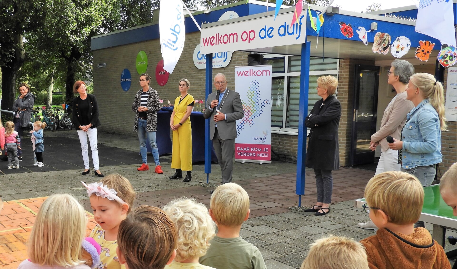 Burgemeester Romeyn opent kindcentrum De Duif samen met kinderen, directie, bestuurders, partners  en medewerkers tijdens het muzikale startfeest.

