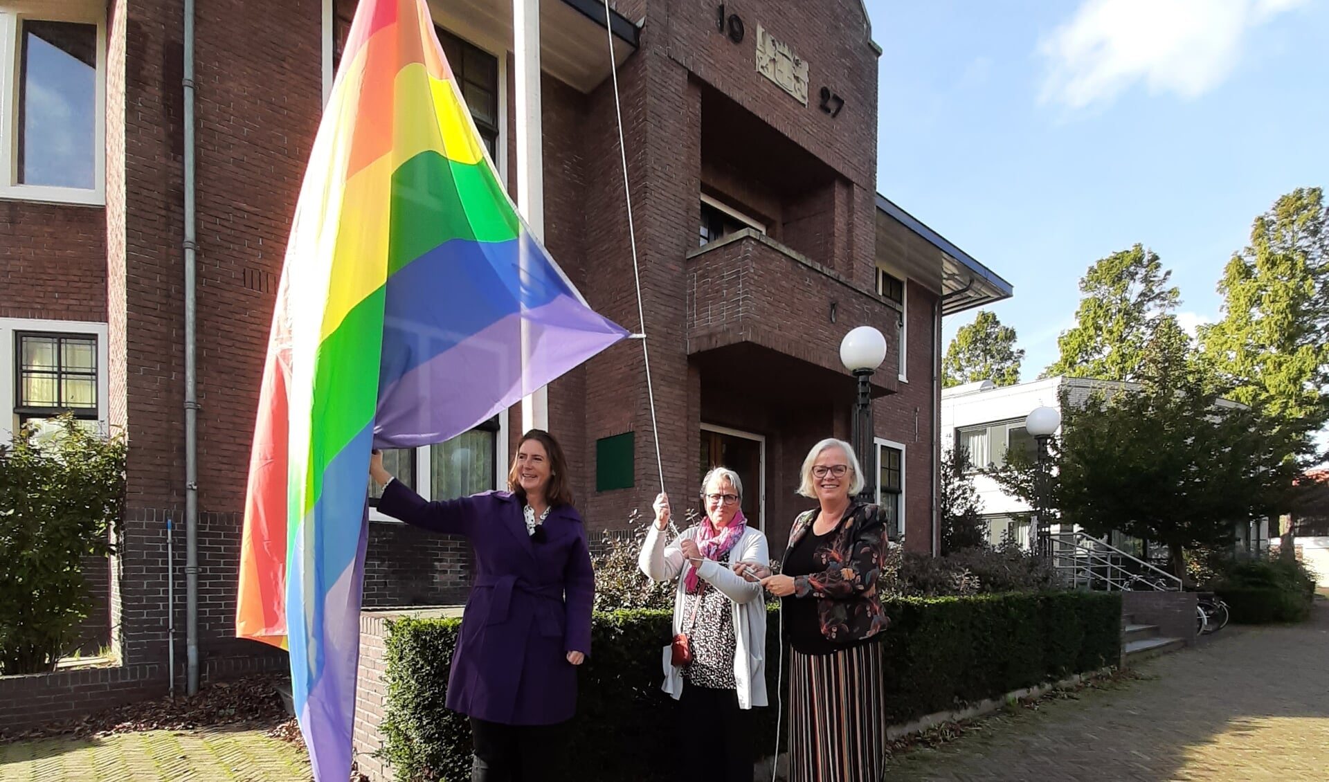 Burgemeester Mascha ten Bruggencate, Dhyan Duijn en wethouder Elly Beens hijsen de regenboogvlag.
