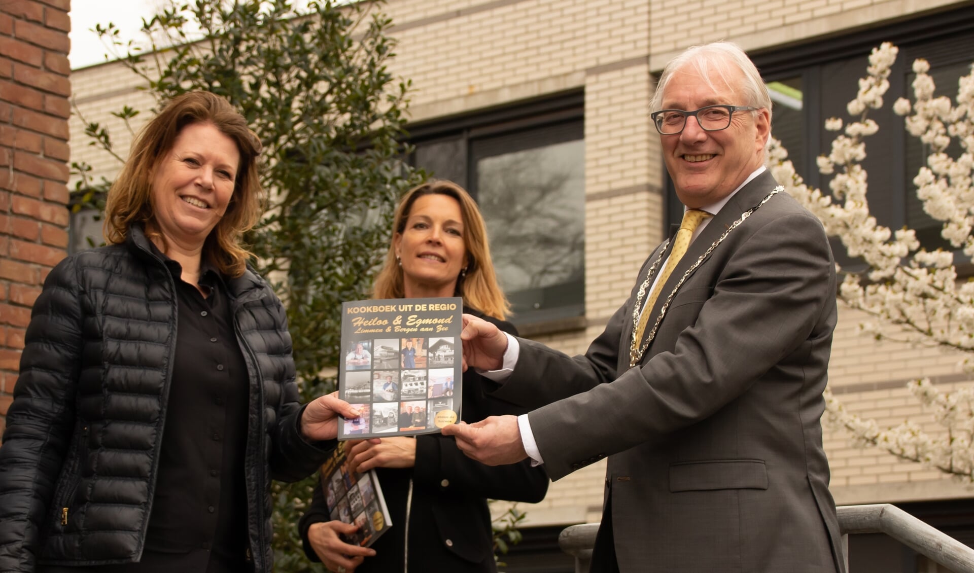 Uitgever Sylvia Blok (l) en Judith Pronk (o.a. sponsorwerving) overhandigen een exemplaar aan burgemeester Romeyn. 