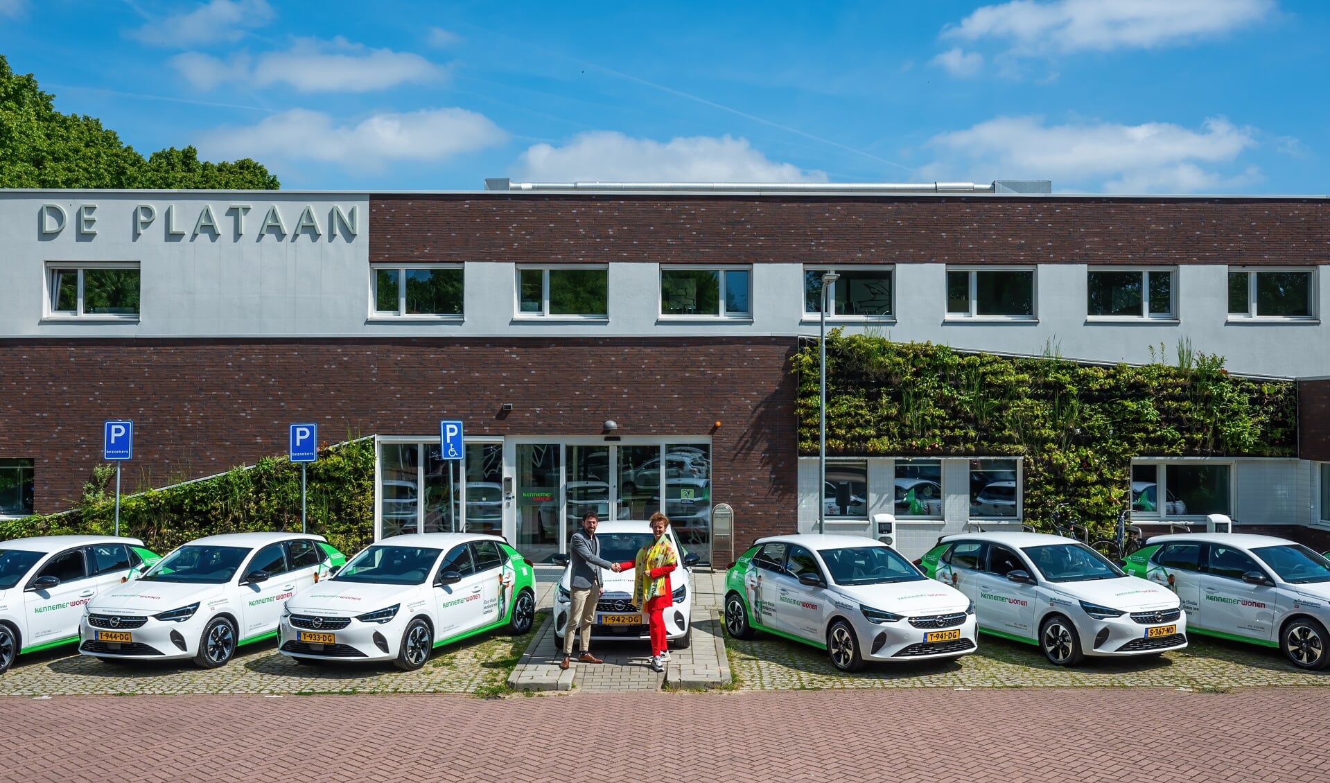 Krista Walter (rechts) neemt acht elektrische Opel Corsa’s in ontvangst van Ruben Elzas voor het kantoor van Kennemer Wonen in Heiloo