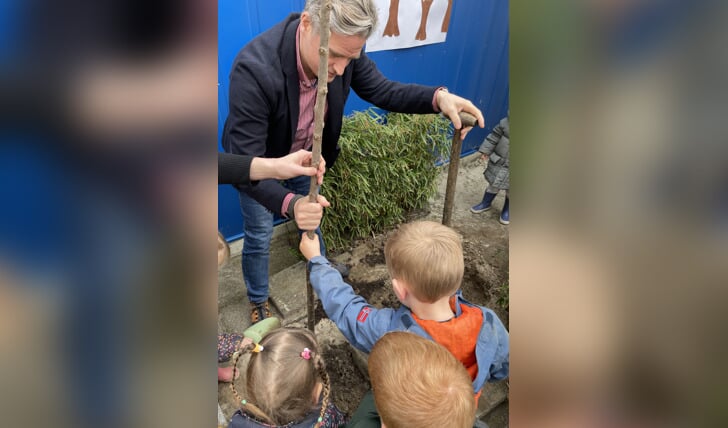 Wethouder Tromp helpt de kinderen bij het planten van een pruimenboom op het plein.
