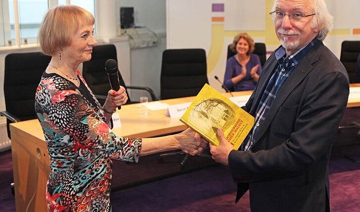 Wethouder Gerrit Pas krijgt het eerste exemplaar van het 'Woordenboek Huizer Dialect' uitgereikt door Ineke van Herwerden. Foto: Bob Awick