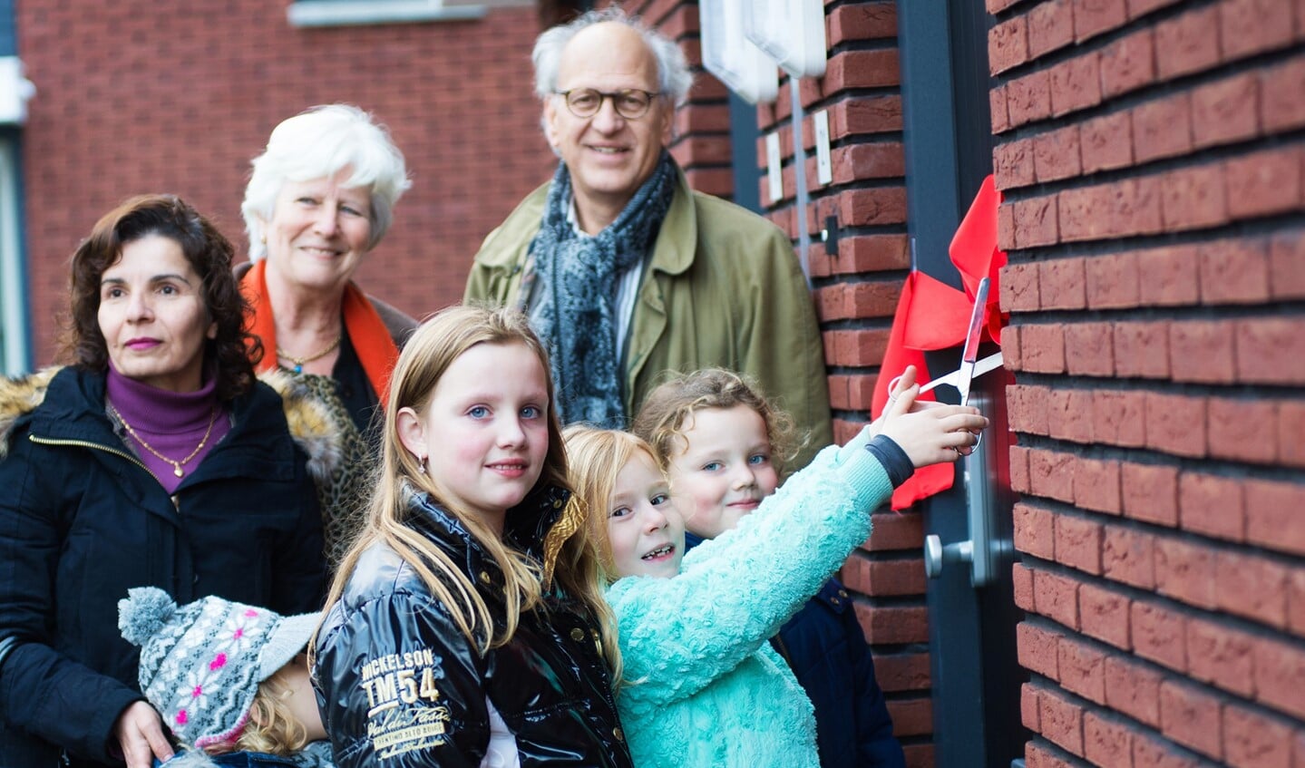De kinderen van het gezin mochten het lintje doorknippen. Op de achtergrond wethouder Anne-Marie Kennis en Pieter Smeijer van Het Gooi en Omstreken.