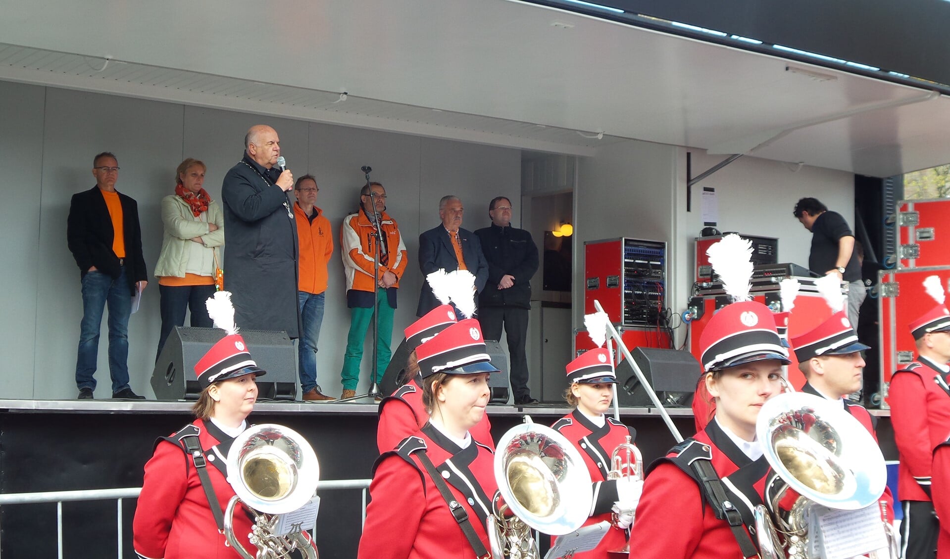 Burgemeester Hertog spreekt de toeschouwers toe. Op de achtergrond het bestuur van de Oranjevereniging.