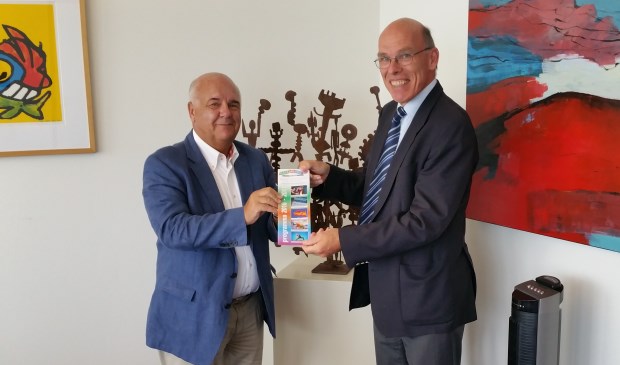 Huizer burgemeester Fons Hertog krijgt de eerste brochure uit handen van Evert de Jong, voorzitter Volksuniversiteit Het Gooi.