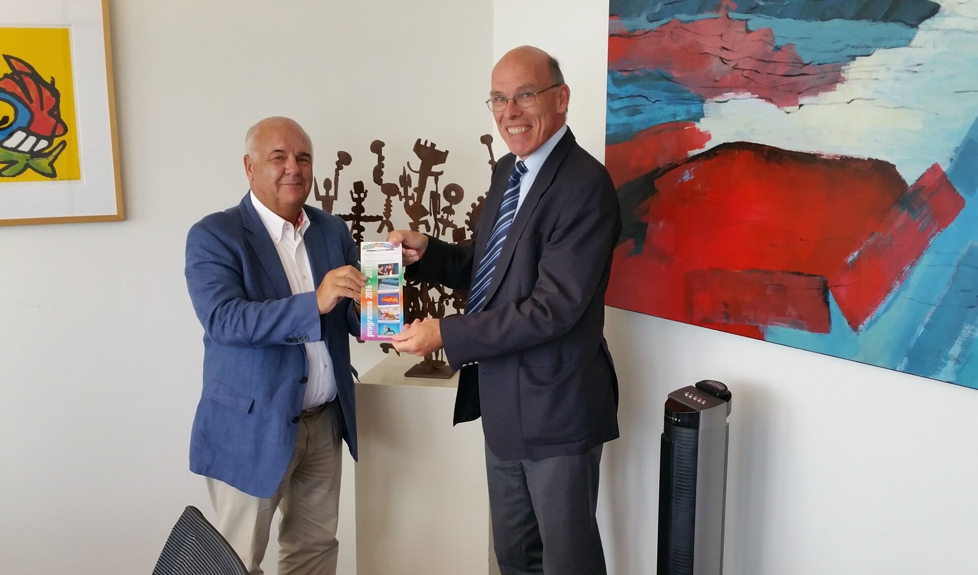 Burgemeester Fons Hertog krijgt de eerste brochure uit handen van Evert de Jong, voorzitter Volksuniversiteit Het Gooi.