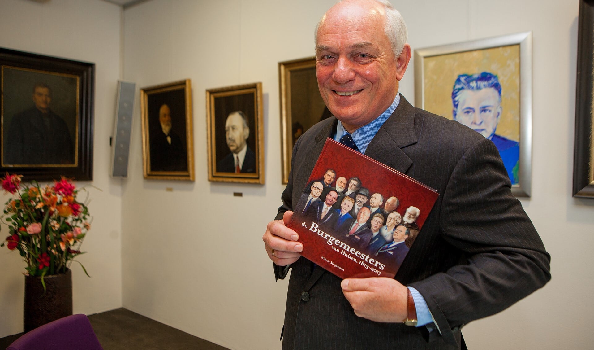 Willem Meijerman met het boek. Achter hem enkele van de burgemeestersportretten.