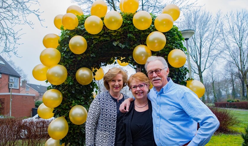 Wethouder Marlous Verbeek samen met het gouden bruidspaar voor de feestelijke boog die de kinderen er vanochtend versierd hebben.