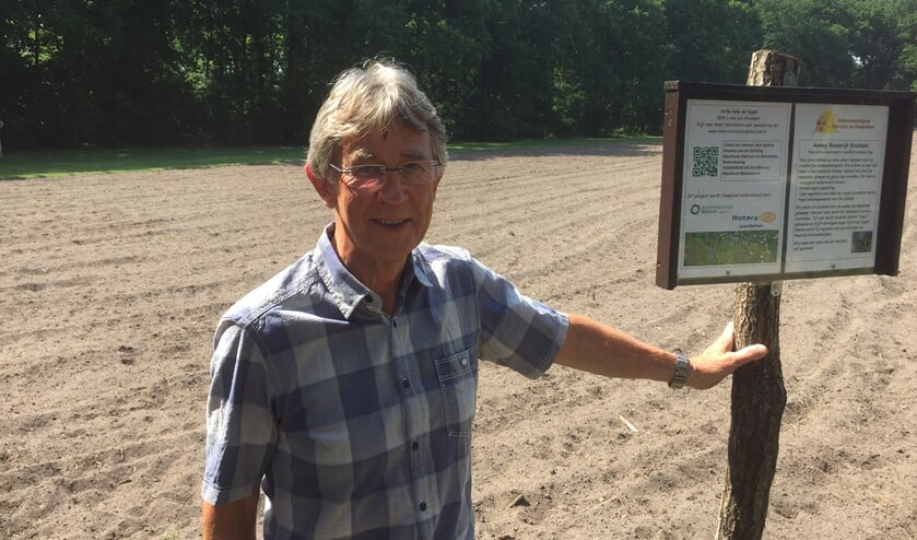 Piet Broeksteeg bij het bord met uitleg over het project op de akker die zal veranderen in bloemrijk grasland.