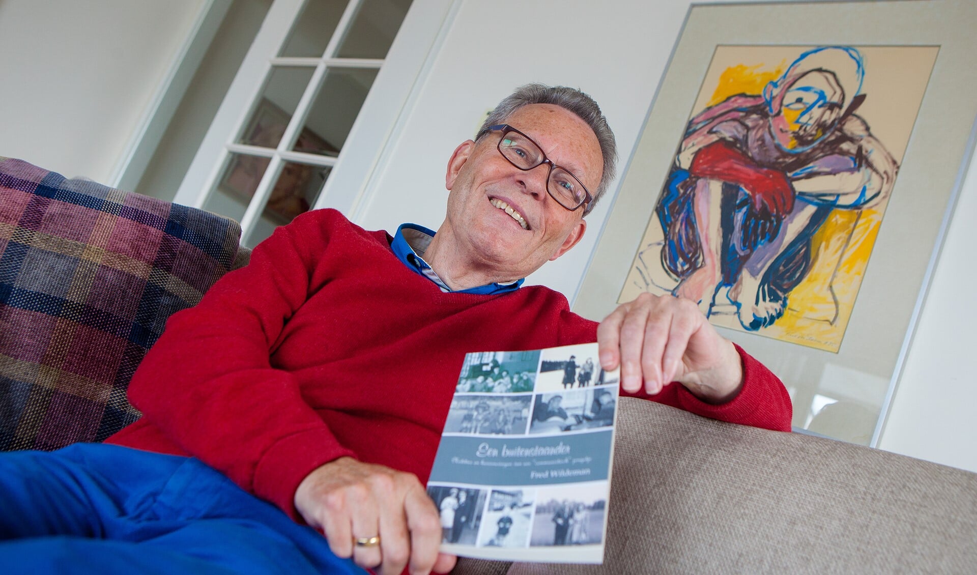Fred Wildeman met zijn boek thuis op de bank in Huizen.