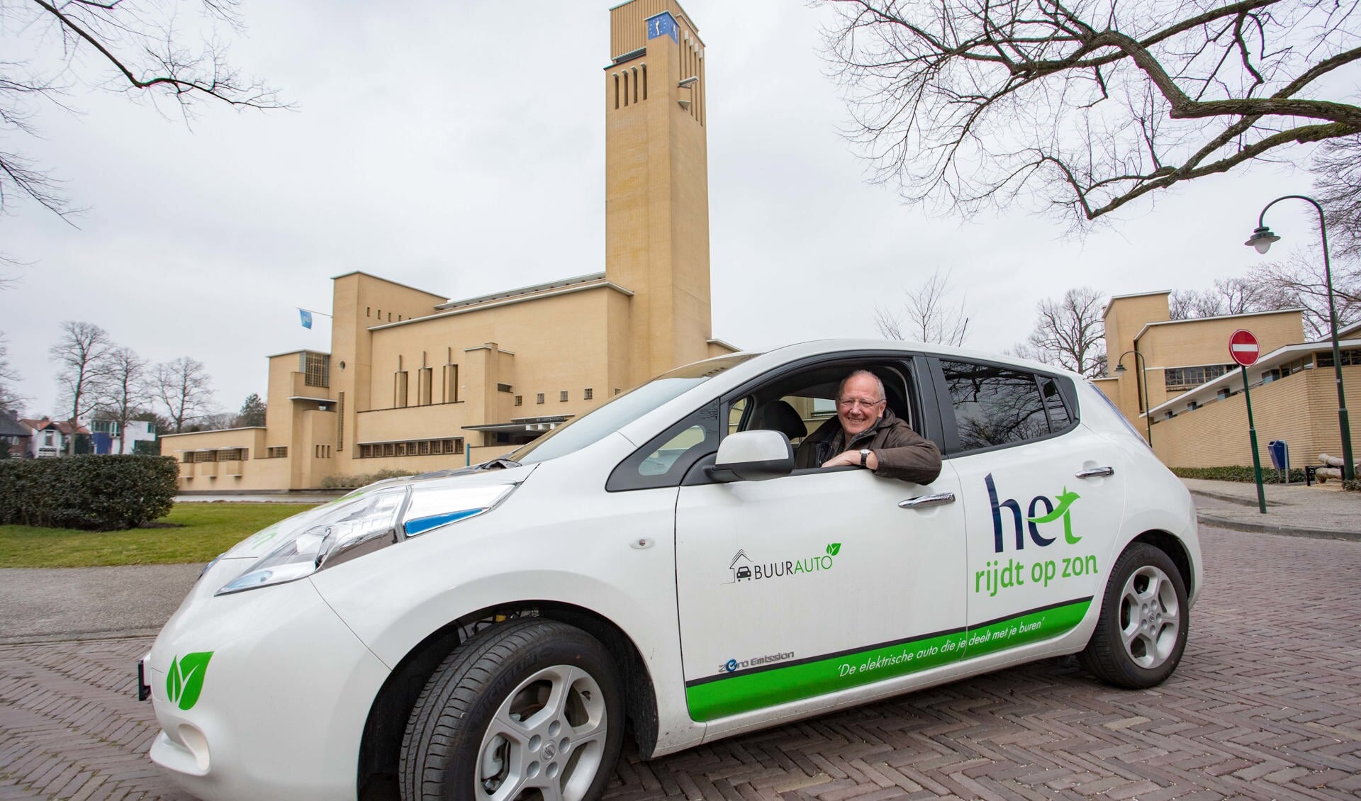Jeroen Pool laat de eerste elektrische deelauto, een Nissan Leaf, van HET zien met het raadhuis als achtergrond.