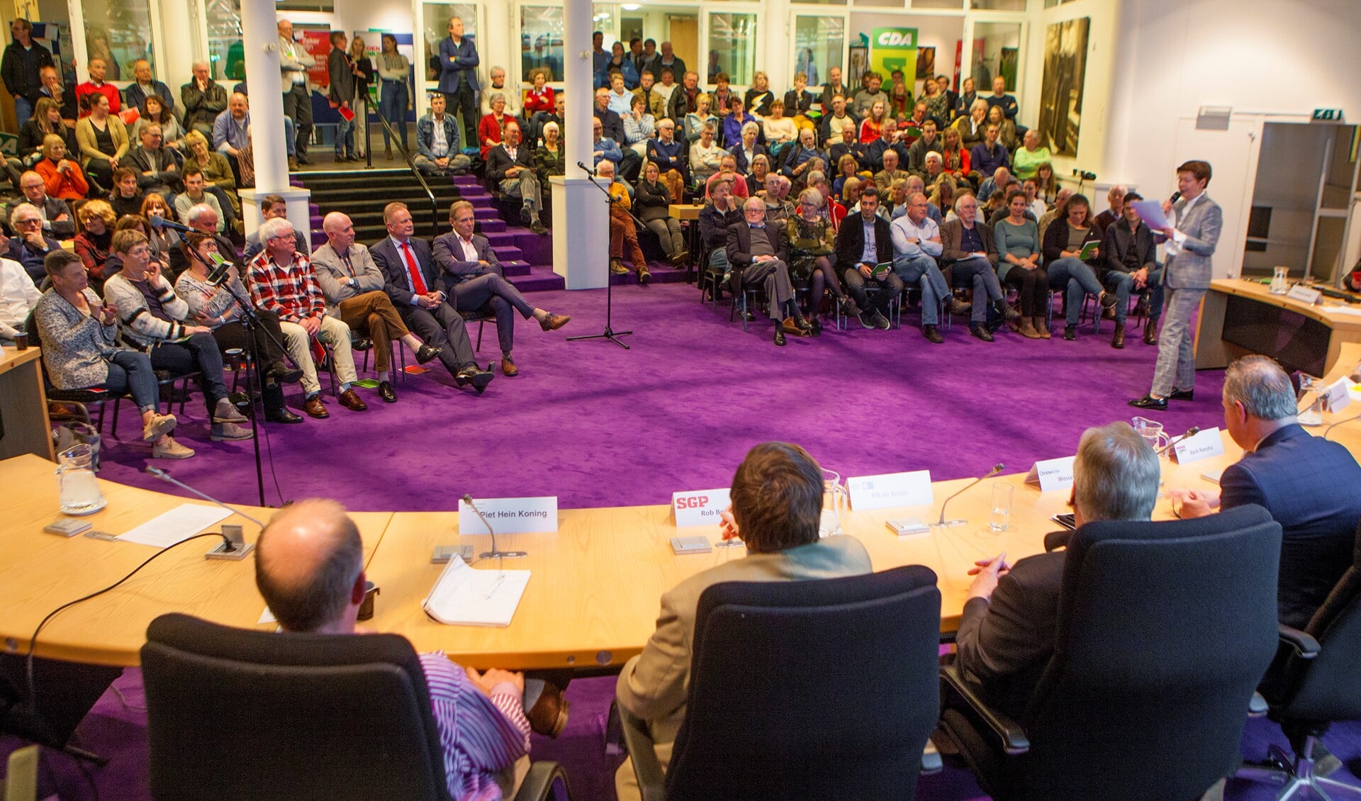 Lijsttrekkers debatteren in de volle raadzaal onder leiding van Maartje van Weegen.