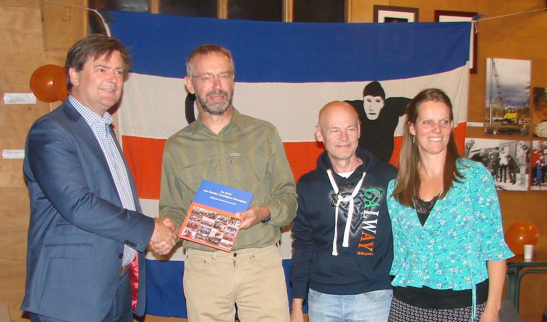 Wethouder Floris Voorink (links) neemt het eerste exemplaar van het jubileumboek in ontvangst uit handen van Marinus Kamphorst vergezeld door medecommissieleden Wim Dral en Anneleen Post.