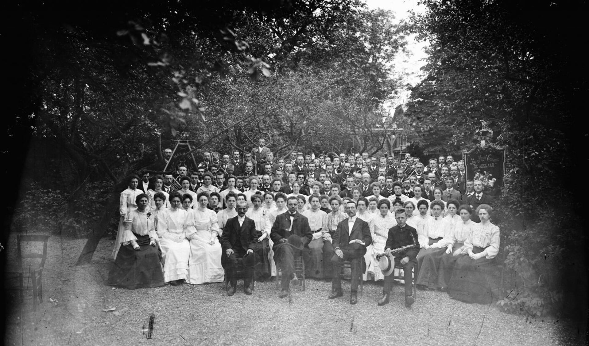 1909 - De leden van het koor en het harmonieorkest poseren met hun instrumenten in een tuin