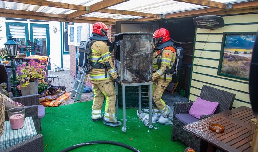 De brandweer draagt het verbrandde apparaat uit de schuur.