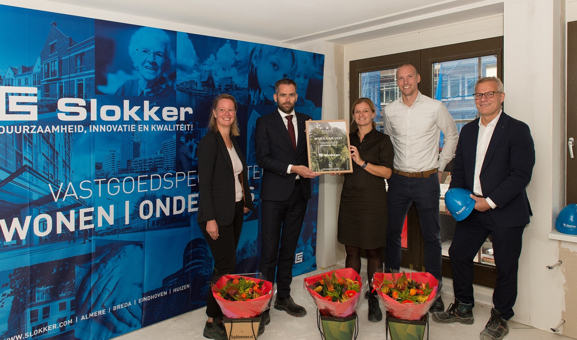 Stefan Wildhagen en Erna Snelder van Slokker nemen het certificaat en de bos bloemen in ontvangst uit handen van Liesbeth Gort, directeur FSC Nederland.