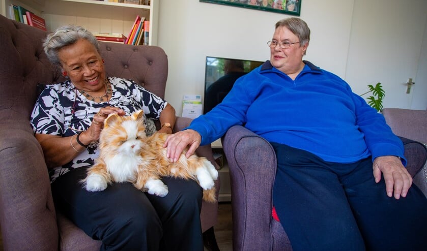 Erica (rechts) aait de robotkat die een lekker plekje heeft gevonden in het Geheugenhuis bij Trui op schoot.