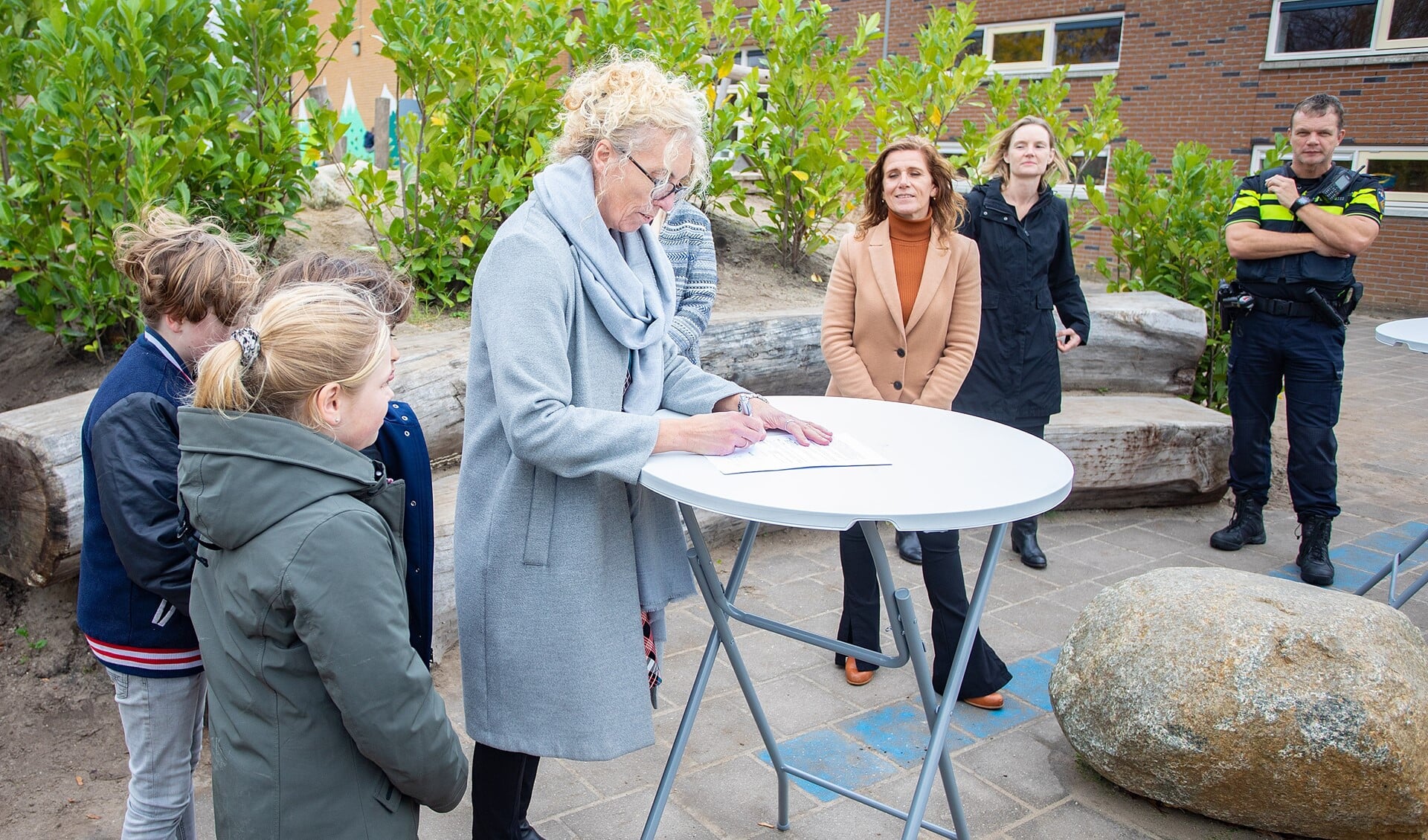 Schooldirecteur Else Linde tekent het convenant Handle with Care onder toeziend oog van haar leerlingen, Veilig Thuis en de politie.