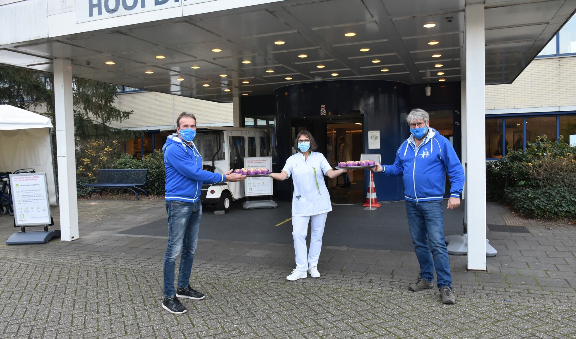 Ton Rigter (links) en Johan Meppelink van Pax kinderhulp Eemnes overhandigen de eerste van de 1.500 muffins aan verpleegkundige Corrie Hartog van Tergooi Blaricum. 