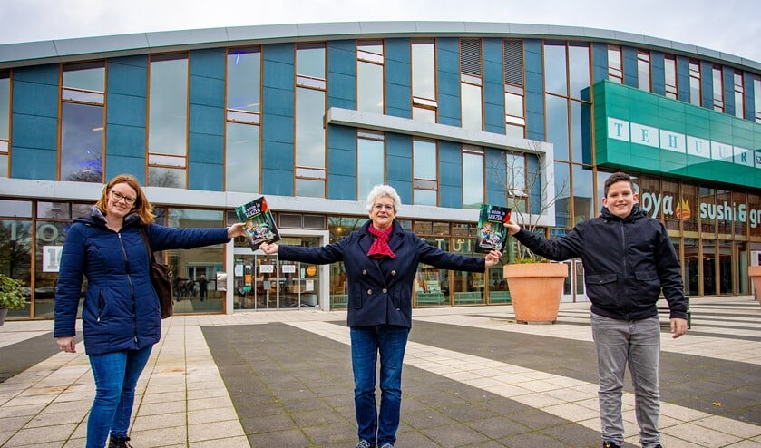 <p>De directeur van de bibliotheek geeft het boek aan een leerkracht en leerling, symbolisch voor de functie van de bieb voor scholen en leerlingen. </p>