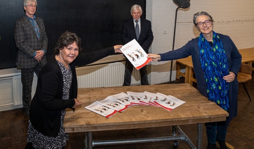 Linda van Versa overhandigt het eerste exemplaar aan wethouder Boudewijnse. Achter Linda staat Huub Jansen van het Beraad en naast hem Jan Stroband van de Seniorenraad.