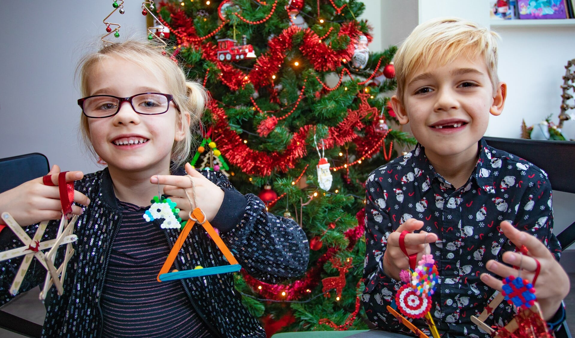 Josefien en Jasper tonen trots enkele zelfgemaakte kerstknutsels voor in de boom.