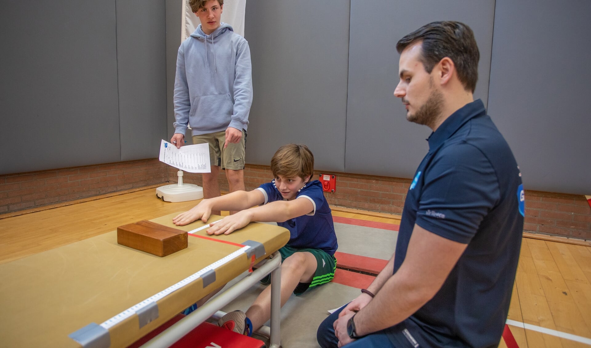 Patrick kijkt toe hoe twee leerlingen een test voor lenigheid afnemen in de gymzaal.