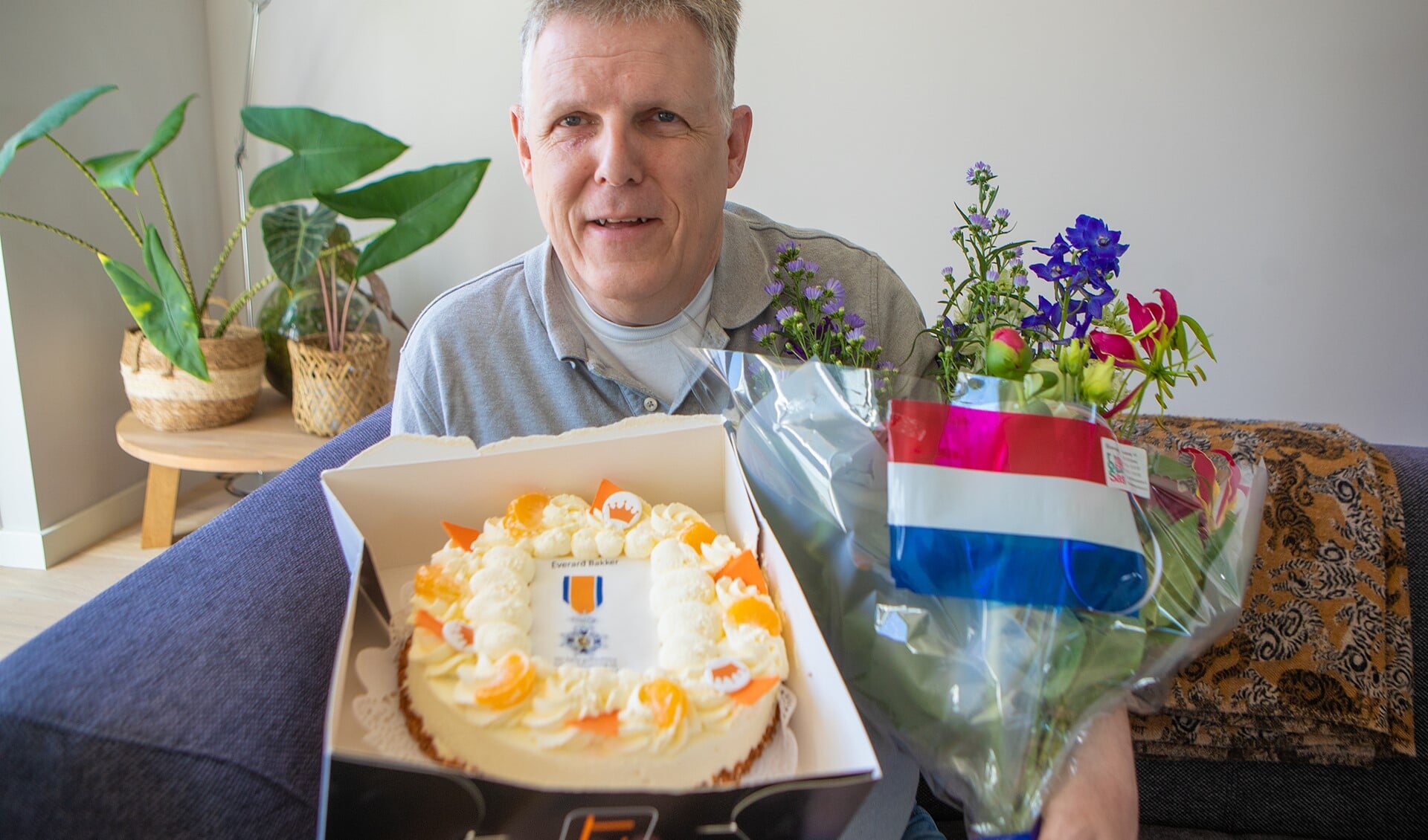De heer Bakker met de bos bloemen en taart die hij kreeg van de gemeente vanwege zijn koninklijke onderscheiding.