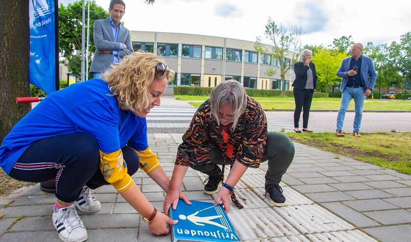 Giselle legt met behulp van Frouck de eerste permanente 'Houd de lijn vrij'-tegel neer. Op de achtergrond kijkt wethouder Maarten Hoelscher toe.