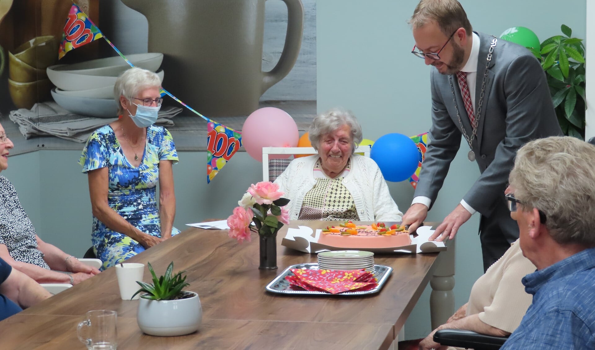De burgemeester snijdt de verjaardagstaart aan voor de 100-jarige Maartje.