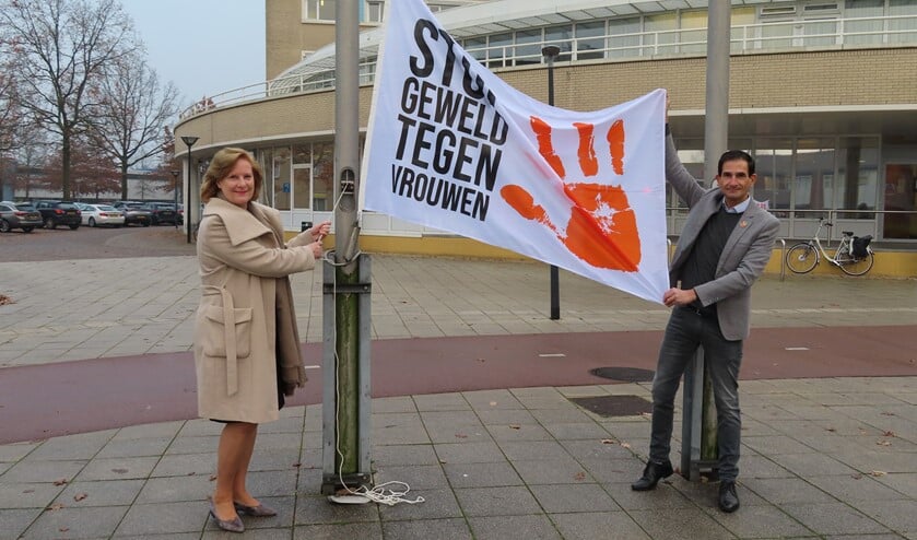 Wethouders Marlous Verbeek en Maarten Hoelscher hijsen de vlag met de tekst 'Stop geweld tegen vrouwen'.