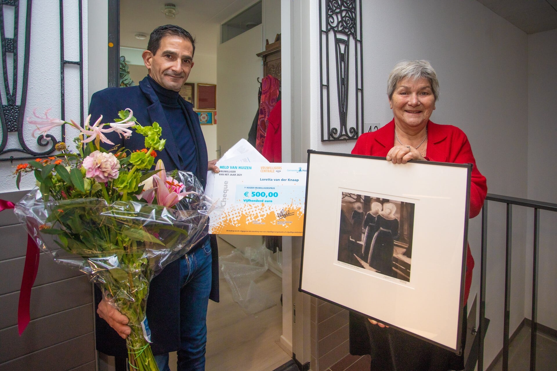 Wethouder Maarten Hoelscher overhandigt winnares Loretta haar prijzen in de hal bij haar huis.