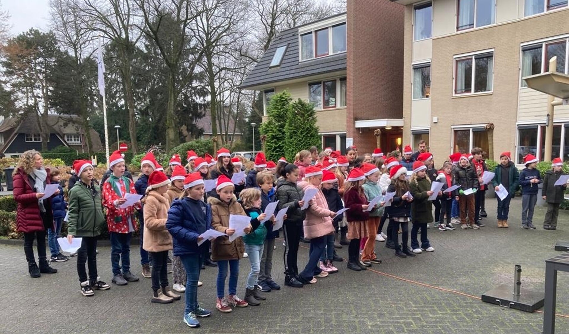 De leerlingen zingen in kerstoutfits de bewoners toe.