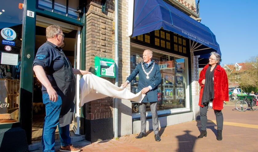 <p>Ondernemer Bleeker en de burgemeester onthullen de aed onder het toeziend oog van wethouder Boudewijnse.</p>