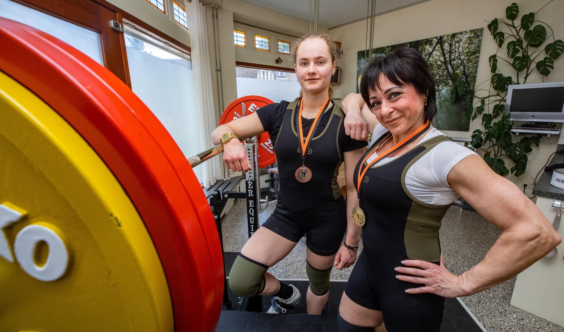Cathelijne Gort (achter) en Christine Rebello laten hun NK-medailles zien in de home gym van de master. 