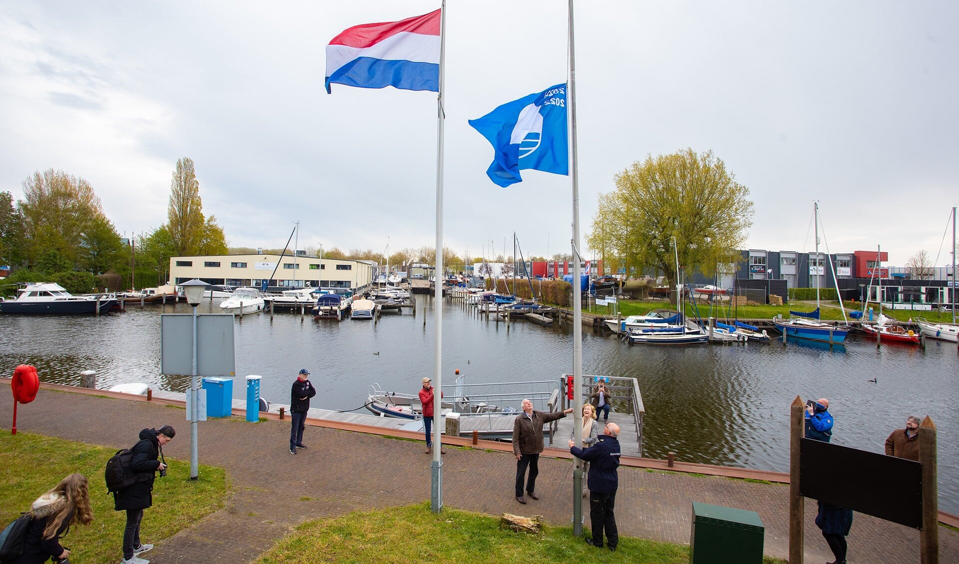 De havenmeester hijst de blauwe vlag in de mast, onder toeziend oog van de wethouder en Patrick Poelmann.