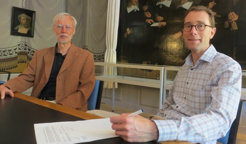 <p>Ben Bakker (l) van de Protestante Gemeente Bussum draagt in de Schilderijenzaal het archief over aan archivaris Niels van Driel.</p>