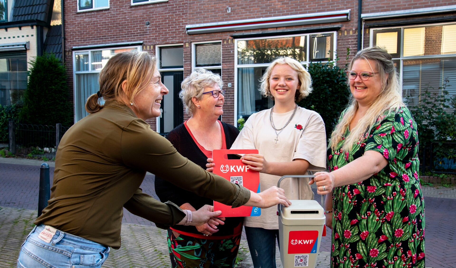 Wijkhoofd Jolanda Karstens (links) organiseert de KWF-collecte in haar wijk en deelt de collectebus uit aan collectant Magda Stomphors. Ze loopt samen met haar moeder Marion en dochter Madelief.