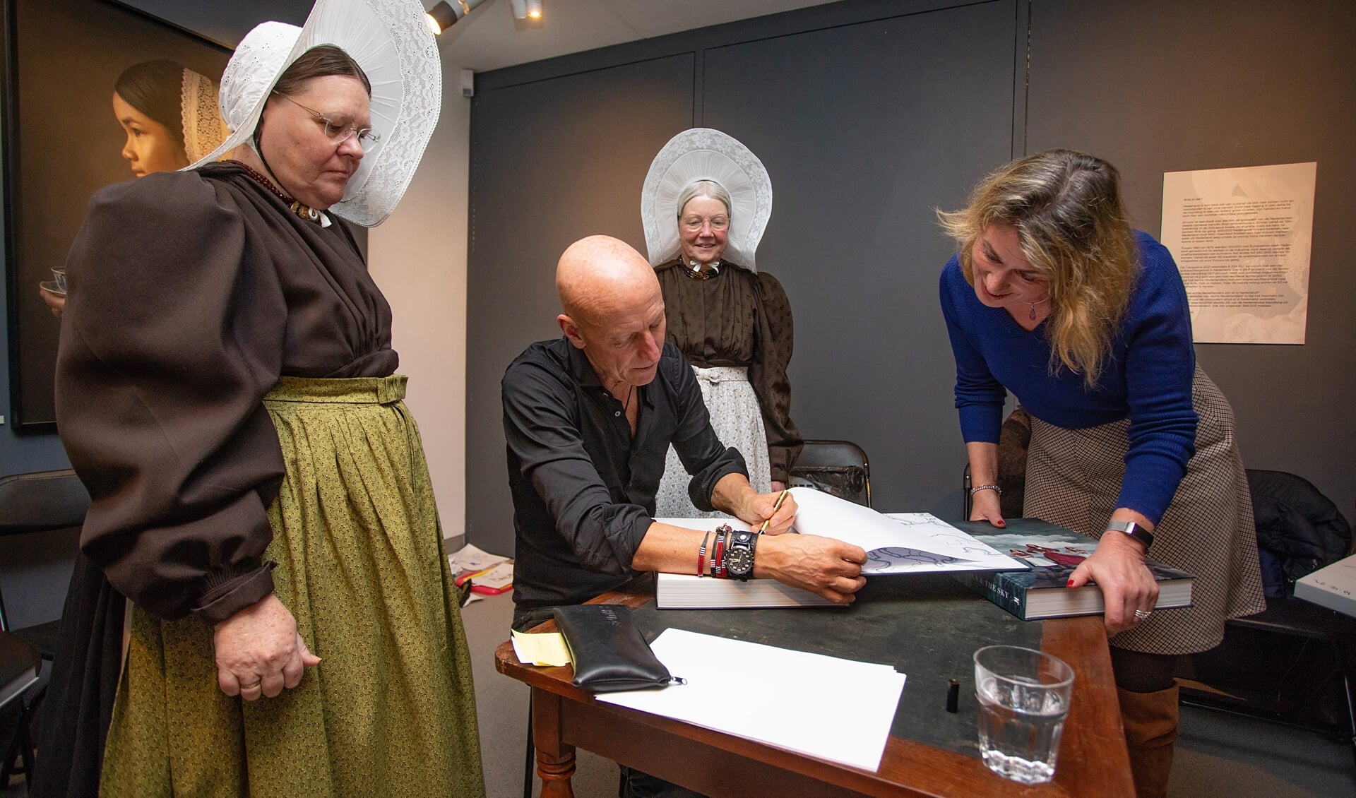 Jimmy Nelson signeert zijn boeken, geflankeerd door de Huizer Klederdrachtgroep.