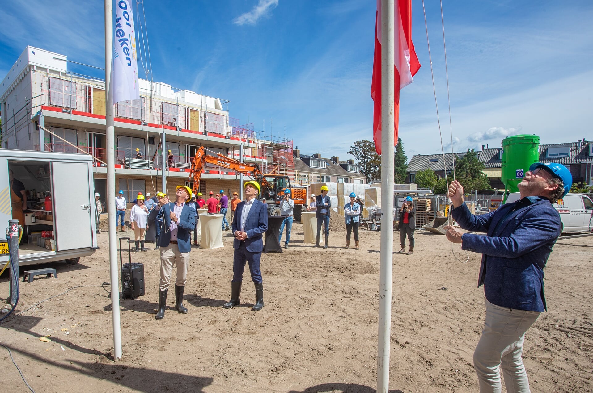 Maarten van Gessel (directeur Het Gooi en Omstreken) en Anno van der Werf (vestigingsdirecteur van Van Wijnen Harderwijk) hijsen de vlaggen, terwijl wethouder Nico Schimmel, de werklui en andere genodigden toekijken.